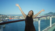© Krakenimages.com - Young hispanic brunette woman with arms outstretched on cruise ship deck railing smiling in sunlight under clear blue sky; joy freedom.
