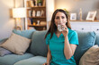 © Jelena Stanojkovic - Female nurse in scrubs relaxing on a sofa at home, smiling and holding a glass of water, enjoying a peaceful break that highlights self-care, hydration and work-life balance.