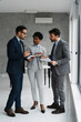 © Novak - Group of three diverse business professionals having a discussion in a modern office, holding and analyzing documents while working on a project together.