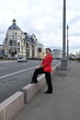 © Шамиль Алиев - A beautiful European-looking girl stands on the side of the road with her foot on the parapet in a big city