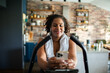 © Davor - Smiling woman using smartphone on stationary bike in home kitchen