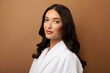 © Home-stock - Beautiful European woman in bathrobe looking at camera, lady with flawless skin standing over beige studio background, closeup portrait