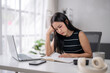 © Wasana - Stressed asian freelancer woman reading notes and working on laptop at home office