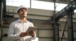 © MdNazim - Man in white shirt and white helmet holding a tablet in an industrial building