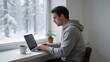 © Sebastian - Man working on laptop by snowy window