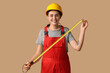 © Pixel-Shot - Young female construction worker with measuring tape on beige background. Woman in male profession concept