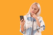 © Pixel-Shot - Thoughtful mature woman with mobile phone on yellow background