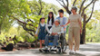 © comzeal - An Asian family enjoys a walk in a lush green park, supporting a senior man in a wheelchair. Multigenerational family authentic love, care, accessibility, and happiness outdoors