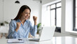 © Athiphat - Happy woman success office laptop business professional achievement motivation celebration career. young woman blue shirt celebrates quietly with small fist pump while looking her laptop