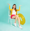 © sitthiphong - Cheerful young Asian woman enjoys her summer vacation, sitting in a deckchair with a yellow rubber ring, raise your hands and be very happy on blue color background