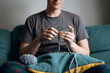 © ADDICTIVE STOCK - Man crocheting on a couch with teal yarn and pillow