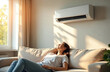 © Vadym - Woman relaxes on sofa near window. Air conditioner cools room on hot summer day. Sunlight streams through curtains, creating shadows on wall. She enjoys fresh cool air.