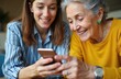 © Vadym - Young woman shows smartphone to happy smiling grandmother. Female teaches elder lady using mobile phone. Family connection with technology. Joyful intergenerational moments at home.
