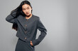 © SHOTPRIME STUDIO - Woman with long black hair wearing gray stylish jacket and skirt posing with hand on hip against neutral background. Fashion model showing contemporary outfit and confident posture.