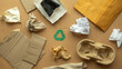 © byjeng - Flat lay of recyclable paper packaging waste with cardboard, envelopes, crumpled paper and green recycle symbol on brown background, eco friendly lifestyle, recycling and zero waste concept.