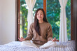 © Farknot Architect - Portrait image of a woman with closed eyes meditating or practicing yoga in lotus pose on the bed