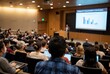 © Meow Creations - Diverse audience listening to presentation in university lecture hall with projection screen