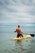 © Aboltin - Athletic man stand up gets on paddleboard and practicing balance and strength. Fitness motivation, healthy body and active lifestyle in natural marine environment