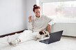 © Tatyana Gladskih - Smiling Young Woman Sitting on carpet and using Laptop by dog at Home