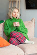 © Tatyana Gladskih - Cute mature Woman wearing knitted clothes enjoying warm tea or coffee indoors home, Woman sitting on sofa