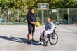 © Koldo_Studio - Two friends with disabilities on a basketball court, one in a wheelchair, the other having a prosthetic leg, holding a ball