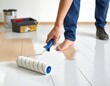 © dika - Person uses a roller to paint a wooden floor white