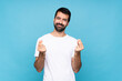 © luismolinero - Young man with beard  over isolated blue background making money gesture