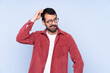 © luismolinero - Young caucasian man wearing corduroy jacket over blue background having doubts while scratching head