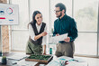 © deagreez - Two colleagues discuss charts and strategy in a bright loft office featuring a moss display and large windows while reviewing documents and planning a business project together