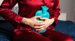 © Iryna - Caucasian woman holding turquoise hot water bottle against abdomen on bed, menstrual pain relief and comfort in bedroom setting