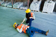© AntonioDiaz - Worker lying on floor after workplace accident, female colleague assisting him in warehouse, safety emergency