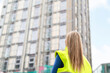 © Iryna - Woman wearing safety jacket stands at construction site observing building work in progress during daylight