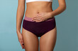 © Home-stock - Woman wearing period underwear gently touching her belly with one hand, expressing awareness of her body during menstruation, blue background