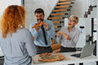 © Novak - Diverse group of happy office colleagues enjoying a pizza lunch break together in a modern workspace