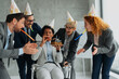 © Novak - Diverse group of business colleagues celebrating a birthday for their African American female coworker as she blows out a candle on a cake in the office.