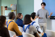 © JackF - During lesson, young man teacher tells material and gives lecture, speaks to group of worker students. Introductory lecture for new staff employees and theoretical introduction to profession