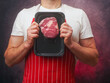 © mark_gusev - Athletic male butcher in white shirt and red and white classic stripe apron showing top quality rib eye steak in vacuum package for extra freshness of the product. Top price beef promotion.