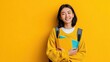 © mila103 - Smiling asian young female student holding notebooks against yellow background.