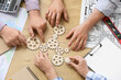 © Pixel-Shot - Hands of engineers with gears on table, top view
