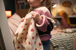 © DragonImages - Caucasian child girl holding up sweater with heart pattern, standing in bedroom, smiling and looking to side, showing excitement while choosing clothing, casual home environment visible