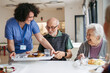 © Halfpoint - Caregiver serving lunch to elderly residents in a care home.