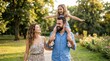 © picture worm - Happy family walking in park,mother and father with daughter on shoulders,summer outdoor lifestyle,parents love,childhood joy,weekend leisure,and togetherness