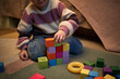 © DragonImages - Caucasian child building colorful block tower on carpet, sitting cross legged and carefully stacking cubes with focused expression, hand placing green block on top of structure