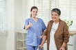 © Ekkasit A Siam - Smiling young asian female physical therapist in blue uniform gives thumbs up while standing beside senior asian female patient holding walker after therapy session in bright clinic