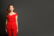 © artmim - Fashionable young woman in red suit standing against black studio wall background