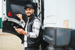 © Serhii - Truck driver smiling using smartphone near commercial vehicle
