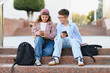 © Serhii - School children sitting on steps using smartphones