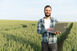 © Serhii - Agronomist using laptop while inspecting wheat field before harvest