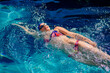 © Connect Images - Swimmer doing backstroke in a vibrant blue pool under sunlight. USA