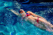 © Connect Images - Woman swimming backstroke in clear blue pool water with sunlight reflecting. USA